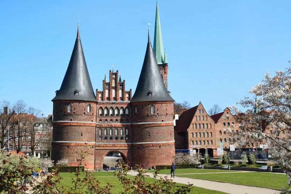 Un grande corpo di guardia storico in mattoni con due torri coniche in un parco verde in una giornata di sole.