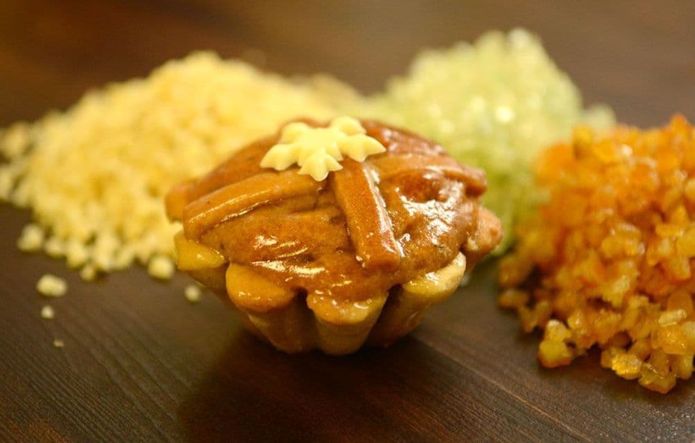 Ein kleines glasiertes Törtchen mit Gitterkruste steht neben farbenfrohen Zuckerstreuseln auf einer Holzoberfläche.