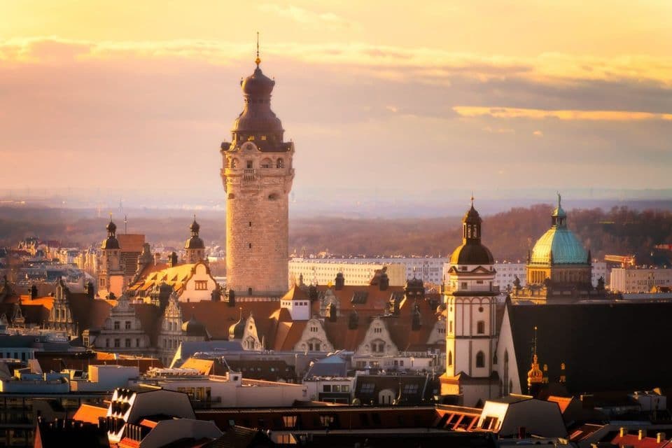Eine historische Stadtsilhouette mit einem markanten Steinturm und verschiedenen Kuppeln, beleuchtet vom warmen Licht eines Sonnenuntergangs.