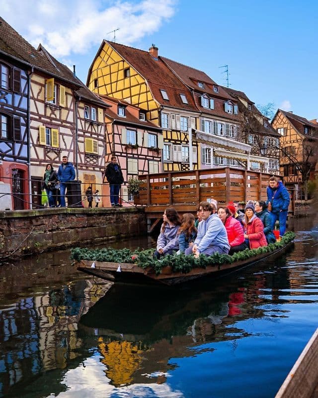 Un viaggio di gruppo WeRoad a bordo di una barca decorata su un canale, tra case colorate a graticcio.