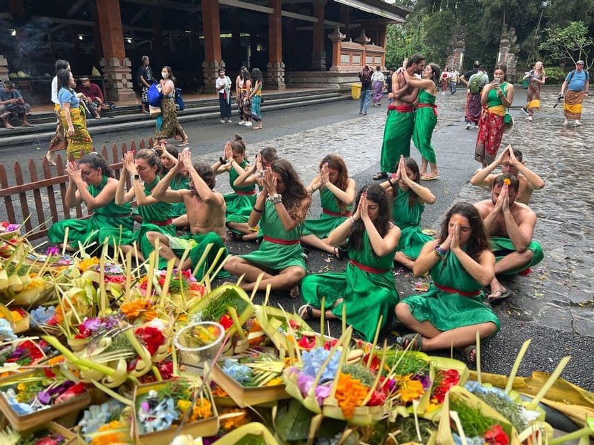 Un grupo de WeRoad vistiendo de verde se sienta en el suelo en posición de oración, con ofrendas florales tradicionales en primer plano.
