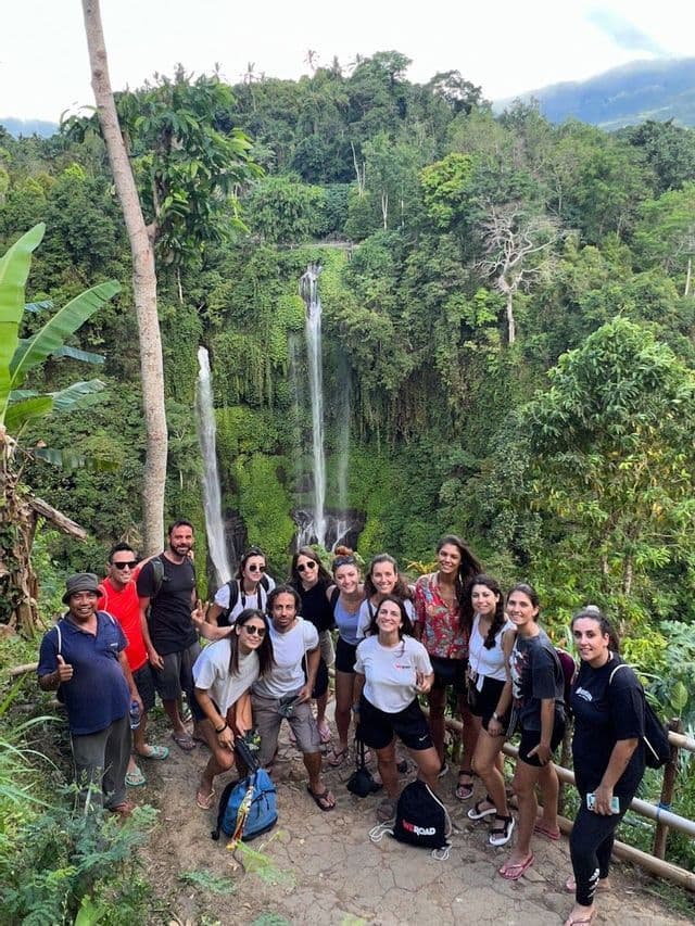 Un gruppo WeRoad in posa per una foto su un sentiero in una giungla lussureggiante, con due grandi cascate sullo sfondo.