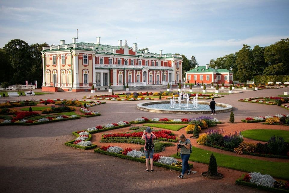 Due persone di un viaggio di gruppo WeRoad visitano gli elaborati giardini di un grande palazzo con una fontana centrale.