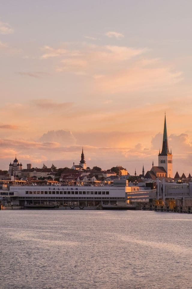 Una città portuale con guglie di chiese e palazzi storici che si affacciano sull'acqua, sullo sfondo di un cielo delicato al tramonto.