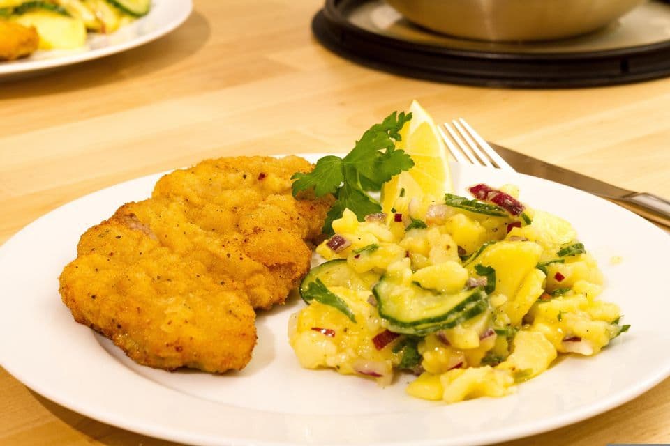 Une assiette de schnitzel pané et de salade de pommes de terre, garnie d'un quartier de citron et de persil, posée sur une table en bois.