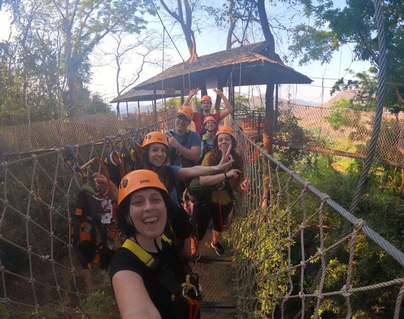 Un viaggio di gruppo WeRoad, indossando caschi e imbracature, si scatta un selfie mentre è in piedi su un ponte di corde sospeso in una foresta.