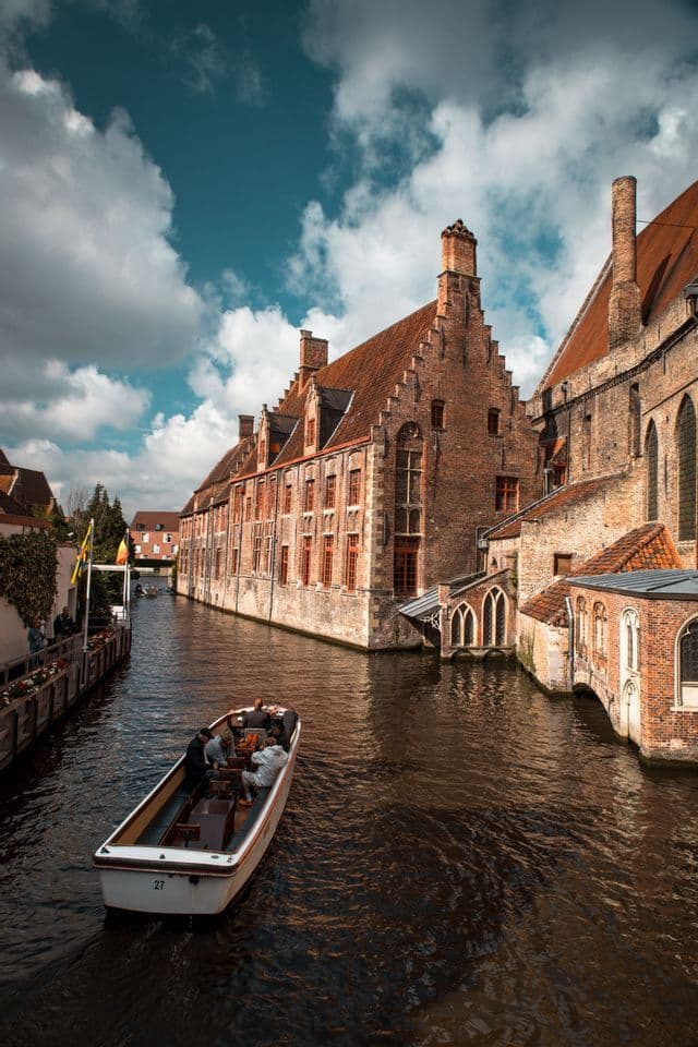 Ein Ausflugsboot mit Passagieren fährt auf einem Kanal entlang, vorbei an historischen Backsteingebäuden mit Giebeldächern, unter bewölktem Himmel.