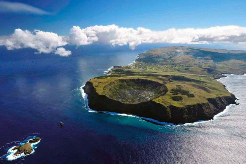 Una vista aerea di un'isola vulcanica verde con un grande cratere, circondata dall'oceano blu profondo sotto un cielo parzialmente nuvoloso.