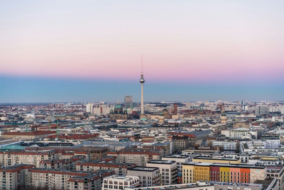 Eine weitläufige Stadtlandschaft mit einem hohen Fernsehturm und einem Kuppeldom unter einem rosa-blauen Himmel bei Dämmerung.