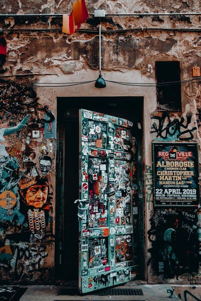 Eine verwitterte Stadtmauer und eine teilweise geöffnete Tür, beide dicht bedeckt mit Aufklebern, Plakaten und Graffiti.