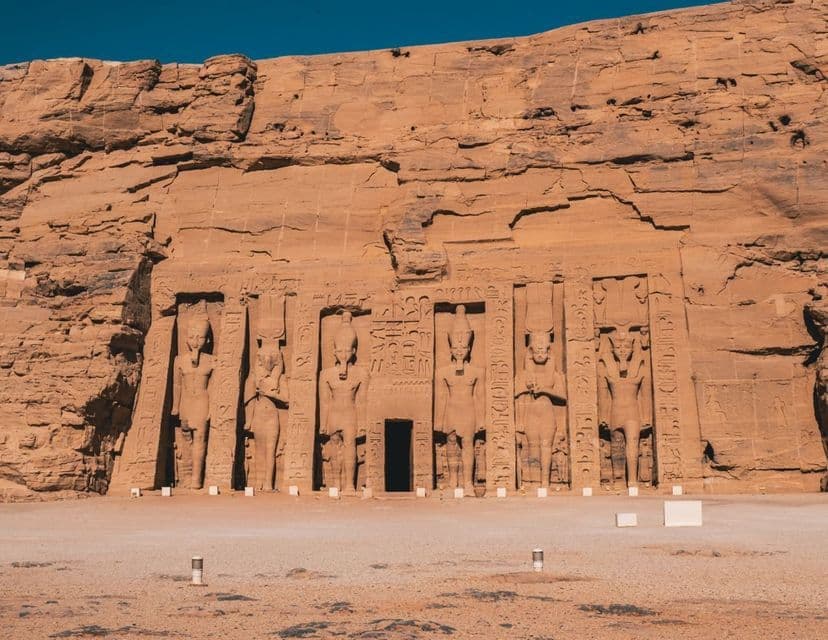 Die Fassade eines großen Tempels, in eine Sandsteinklippe gehauen, mit kolossalen Statuen und Hieroglyphen, die einen zentralen Eingang flankieren.