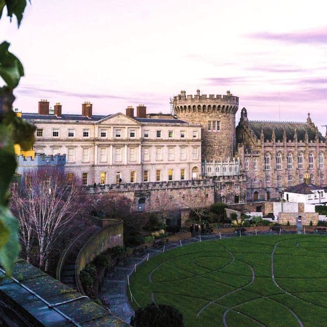 Ein historischer Burgkomplex mit Turm und gepflegtem kreisrundem Rasen, von oben bei Sonnenuntergang unter violettem Himmel gesehen.