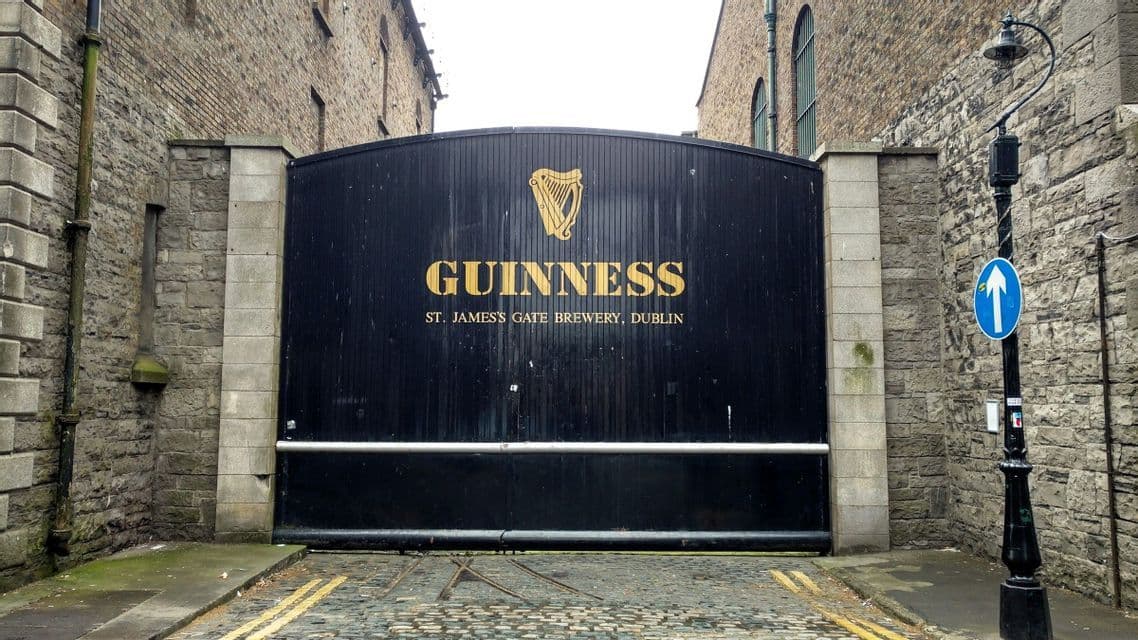 Das schwarze Eingangstor zur Guinness St. James's Gate Brauerei in Dublin, eingebettet zwischen zwei Steingebäuden an einer Kopfsteinpflasterstraße.