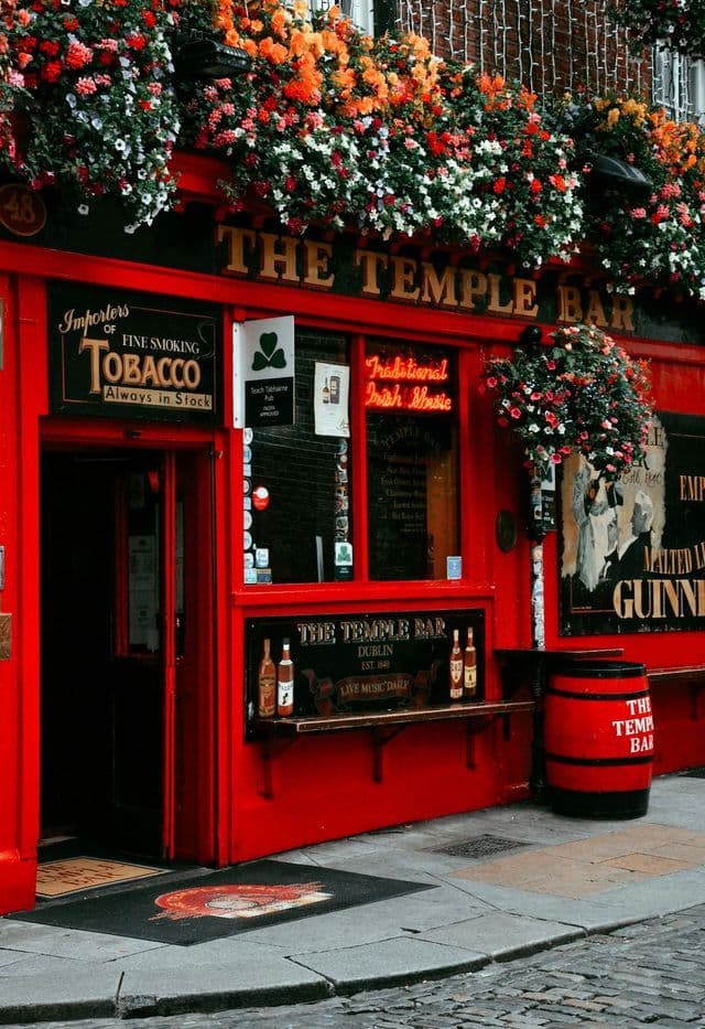 Die leuchtend rote Fassade des The Temple Bar Pubs, geschmückt mit zahlreichen bunten Blumen über Eingang und Fenstern.