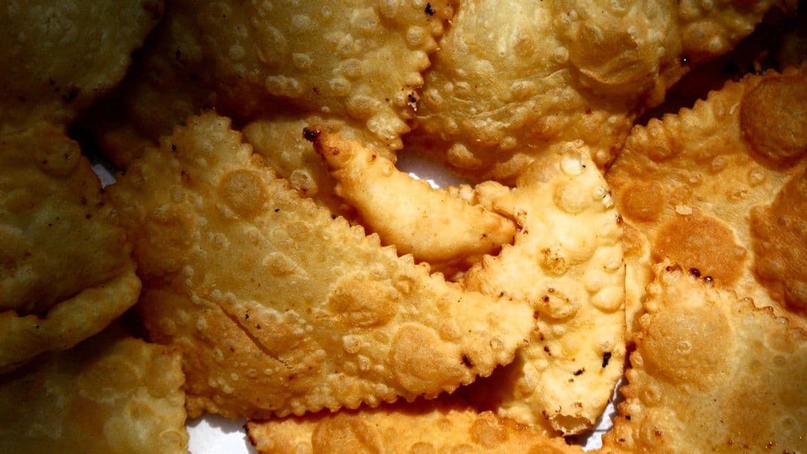 Eine Nahaufnahme von mehreren goldbraunen, frittierten Gebäckstücken mit gekräuselten Rändern, die übereinander gestapelt sind.