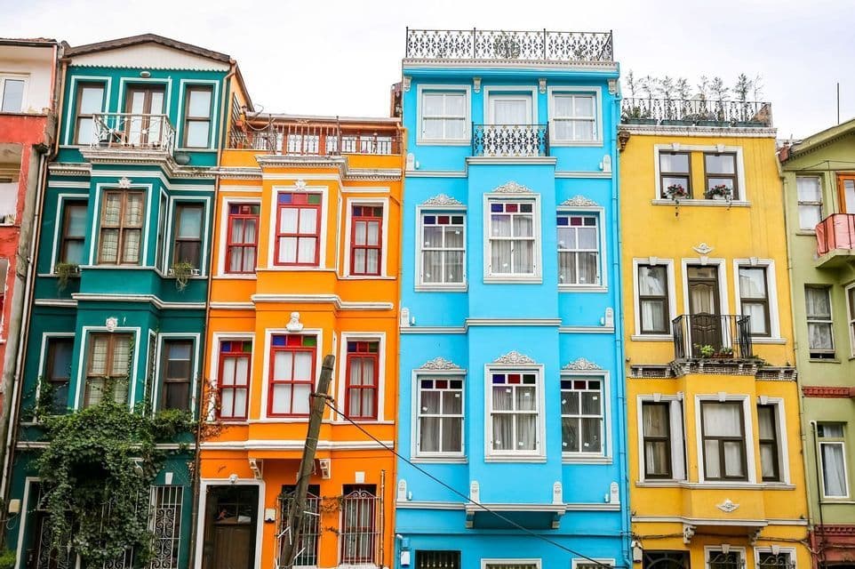 Una fila di edifici stretti e a più piani, dipinti in vivaci tonalità di verde acqua, arancione, blu e giallo.