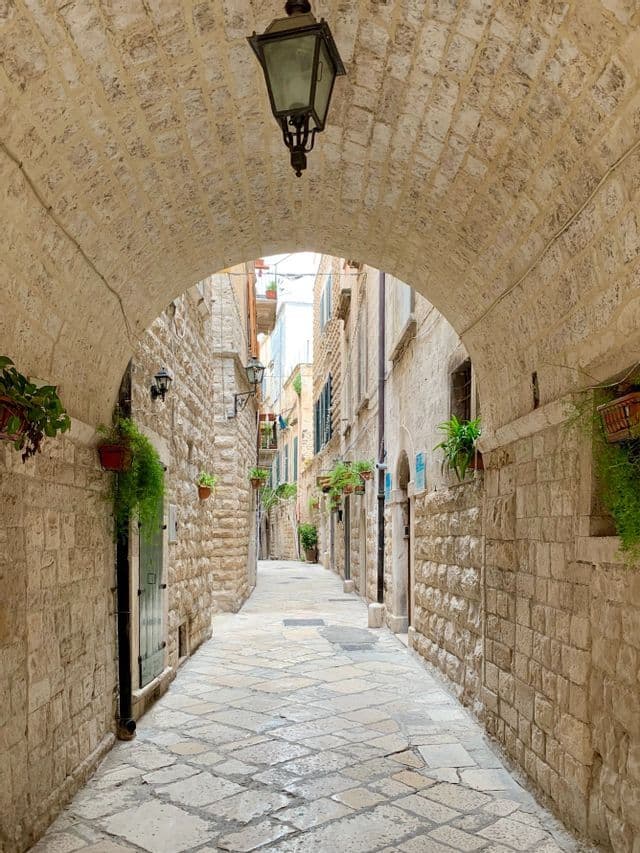 A view down a narrow, empty cobblestone street framed by a stone archway with a hanging lantern.