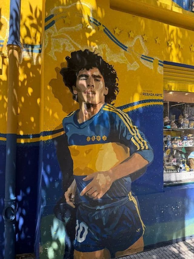 Un murale colorato di Diego Maradona, calciatore, dipinto su una parete di un edificio in blu e giallo.