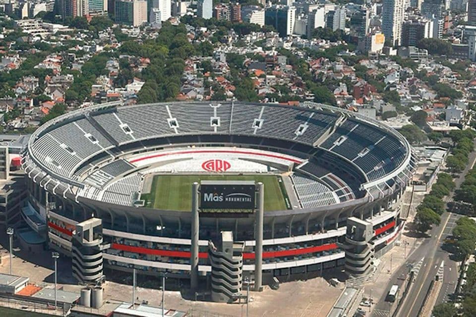 Vista aerea diurna del massiccio e circolare stadio di calcio Mâs Monumental circondato da un denso paesaggio urbano.