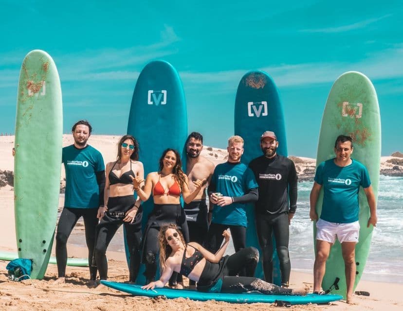 Un gruppo WeRoad di otto persone in muta in posa con le loro tavole da surf su una spiaggia sabbiosa.