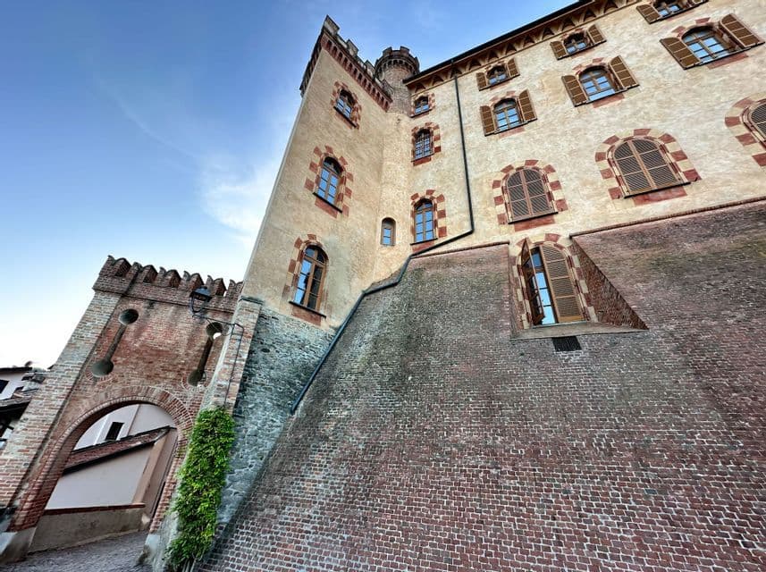 Un'inquadratura dal basso di un castello storico con mura in mattoni, finestre ad arco con persiane e un portale fortificato sotto un cielo azzurro.