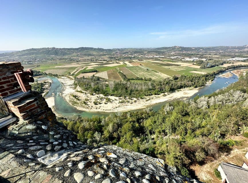 Una veduta aerea di un fiume turchese che serpeggia in una valle con campi a mosaico e foreste sotto un cielo sereno.