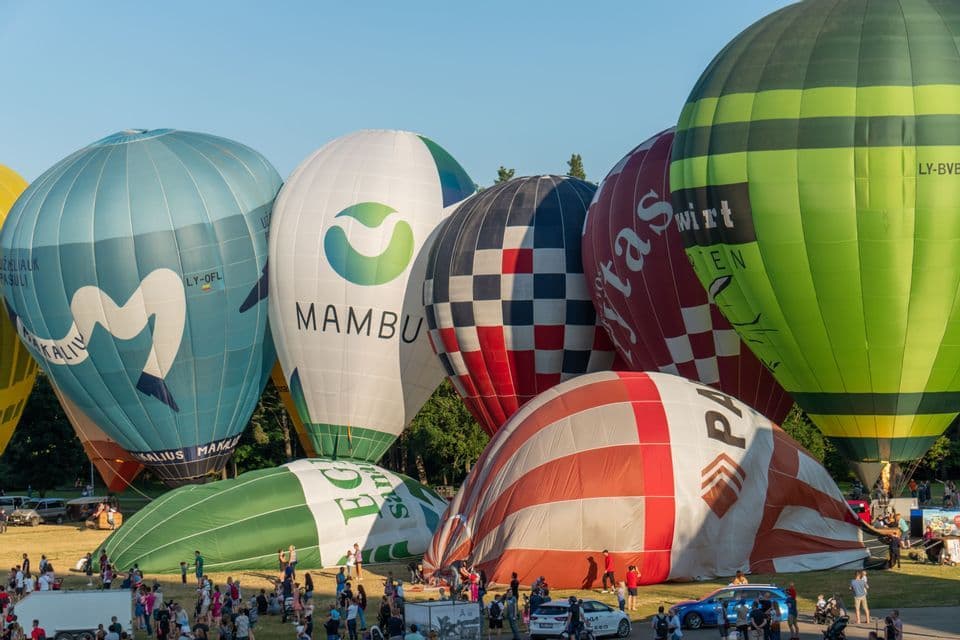 Molte mongolfiere colorate vengono gonfiate e preparate su un prato con una folla di persone che osserva.