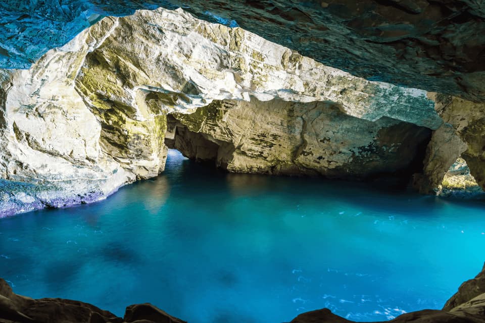 Vista dall'interno di una grotta marina, che mostra acque turchesi brillanti che scorrono tra formazioni rocciose frastagliate.