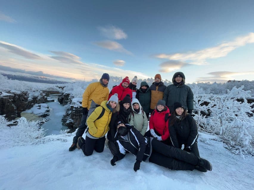 A WeRoad group trip posing for a photo in a snowy landscape next to a frozen river canyon at sunrise.