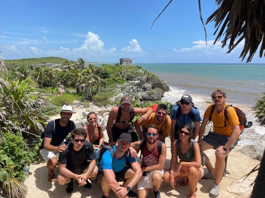 Un viaje en grupo de WeRoad posando para una foto en un acantilado con vistas a una playa tropical con ruinas antiguas y palmeras.