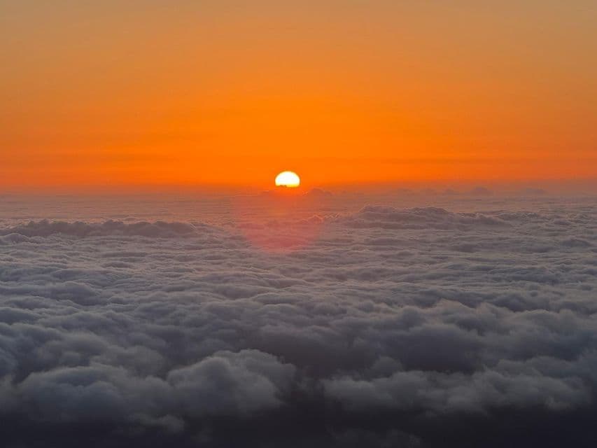 Il sole arancione brillante tramonta all'orizzonte sopra una densa coltre di nuvole bianche e grigie, visto dall'alto.