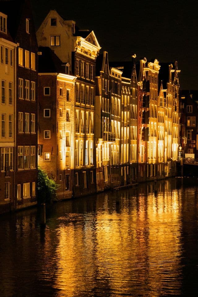Una fila di tradizionali case sul canale illuminate di notte da una luce dorata, che riflettono sull'acqua.
