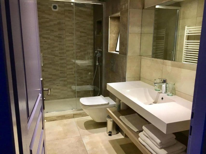 Une salle de bain moderne avec des murs carrelés beiges et marron, comprenant une douche à l'italienne en verre, un WC suspendu et une vasque blanche.