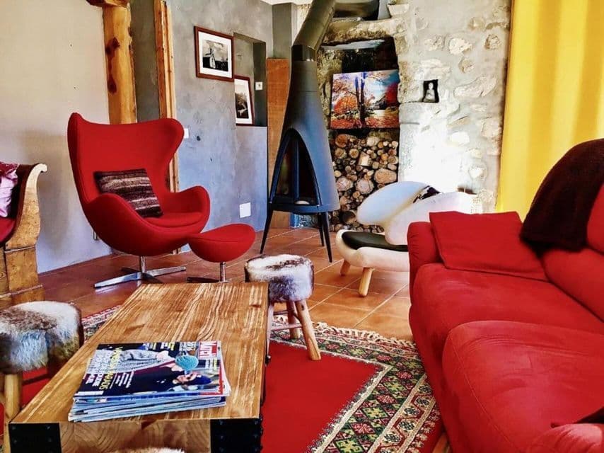 Un salon rustique avec des meubles rouges, une cheminée noire moderne, une table basse en bois et un mur en pierre.