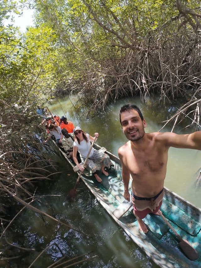 Ein Mann macht ein Selfie, während eine WeRoad-Gruppe mit einem schmalen Kanu durch einen dichten Mangrovenwald paddelt.