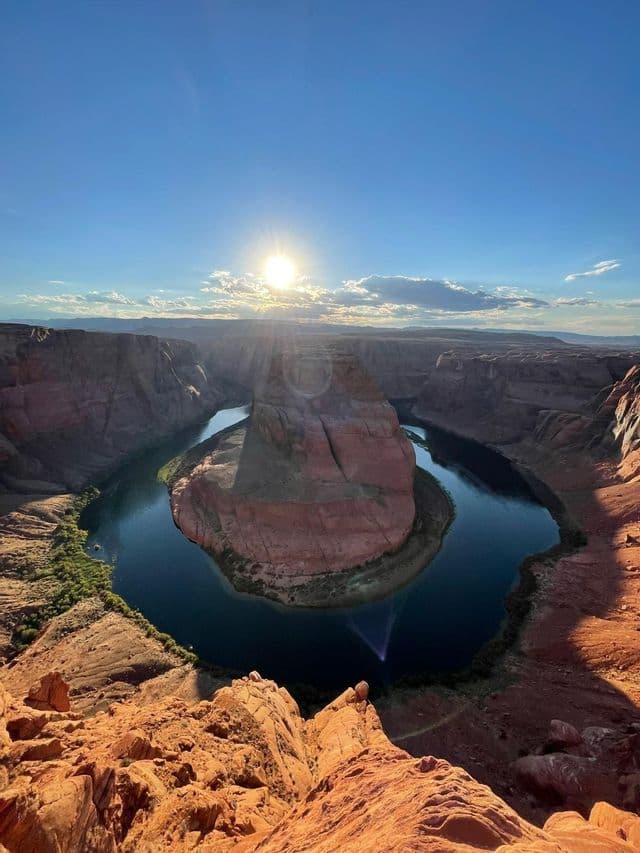 A high-angle view of a river forming a horseshoe bend through a red rock canyon under a bright, sunny sky.