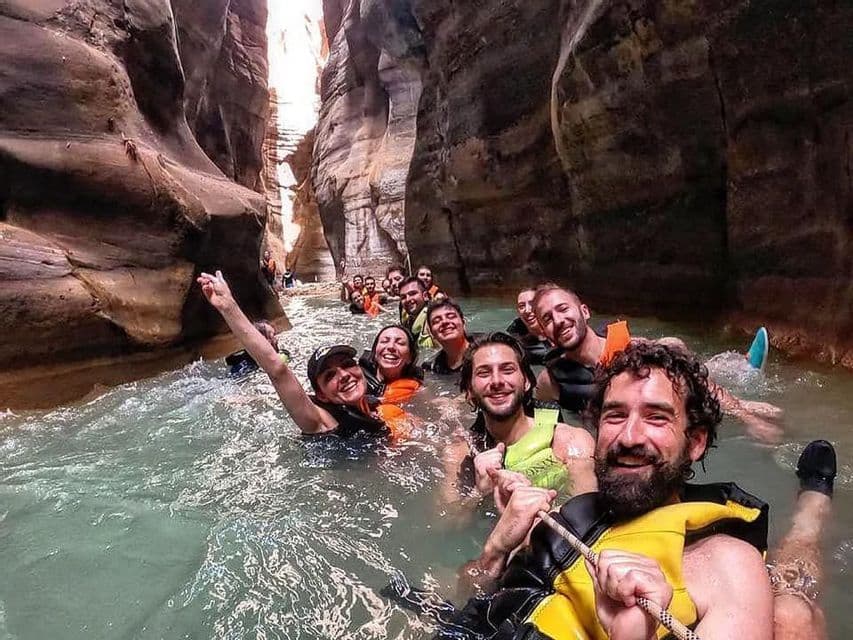 Un groupe WeRoad sourit pour une photo en flottant dans l'eau à travers un canyon rocheux étroit.