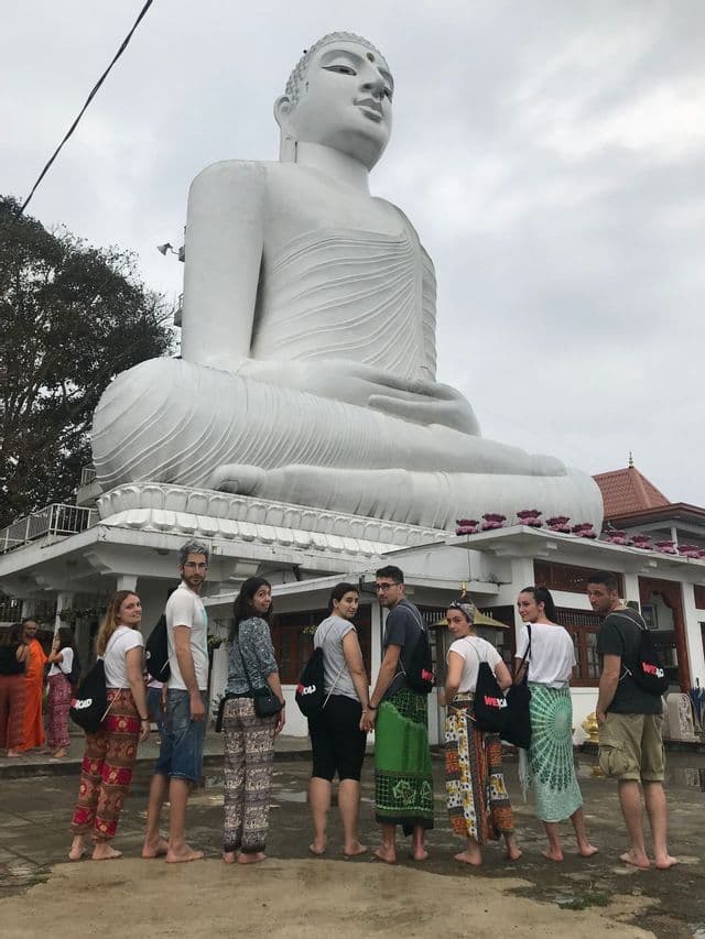 Eine WeRoad-Gruppenreise posiert barfuß vor einer riesigen weißen sitzenden Buddha-Statue in einem Tempel.