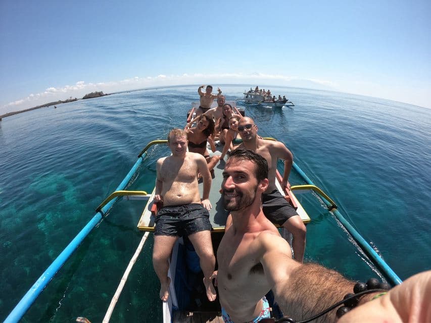 Un grupo de WeRoad se toma una selfie en una barca estrecha mientras navega sobre aguas turquesas cristalinas en un día soleado.