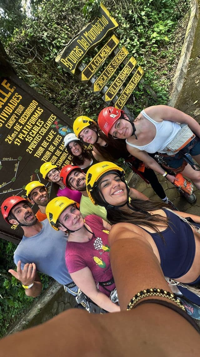 Un groupe WeRoad de personnes souriantes, portant des casques et des harnais colorés, prend un selfie dans la jungle.