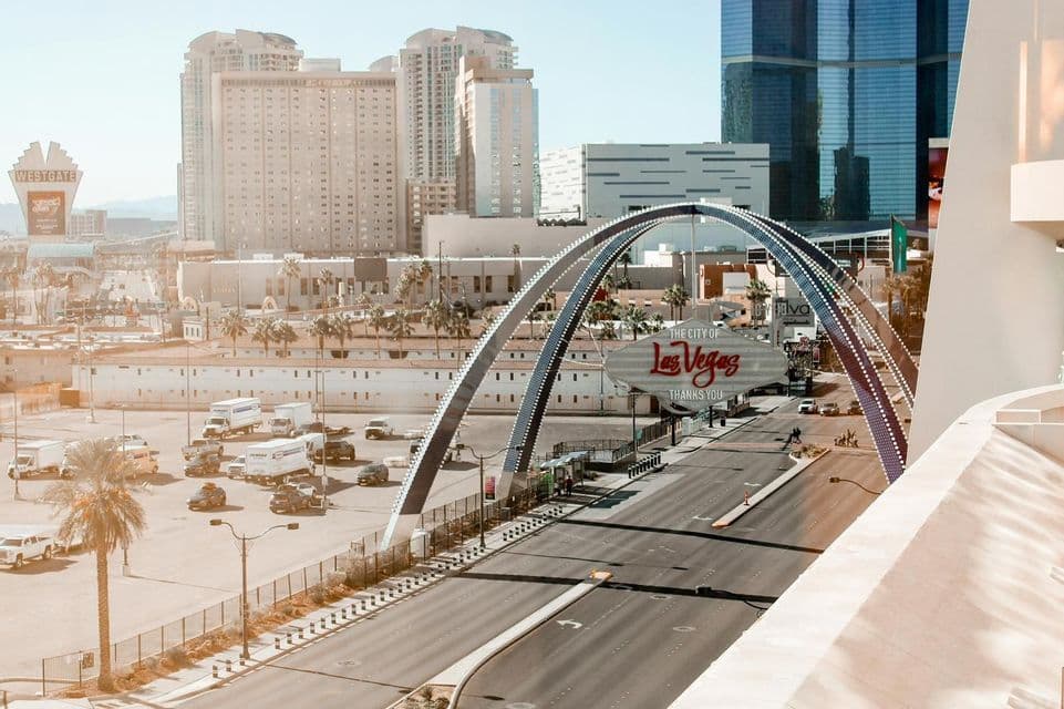 A large arch spans a road by 'The City of Las Vegas' sign, with hotels and the city skyline visible in the background.