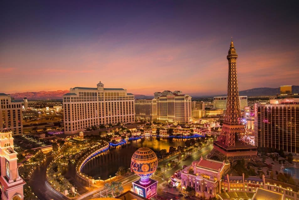 An aerial view of the Las Vegas strip illuminated at dusk, featuring a replica of the Eiffel Tower next to casinos and hotels.