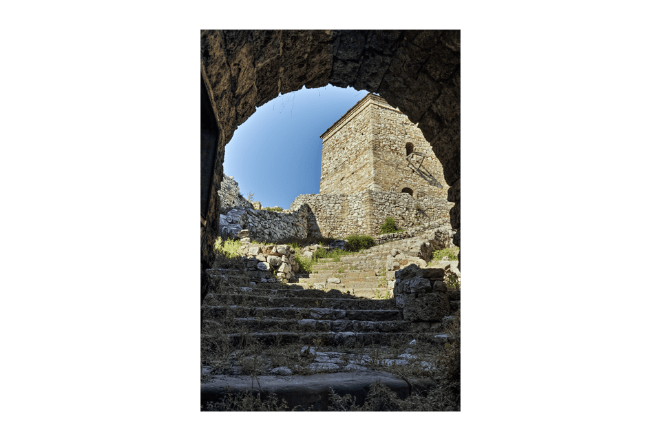 Scalini in pietra consumati portano a una storica torre di avvistamento, visti dall'interno di un oscuro arco in pietra.
