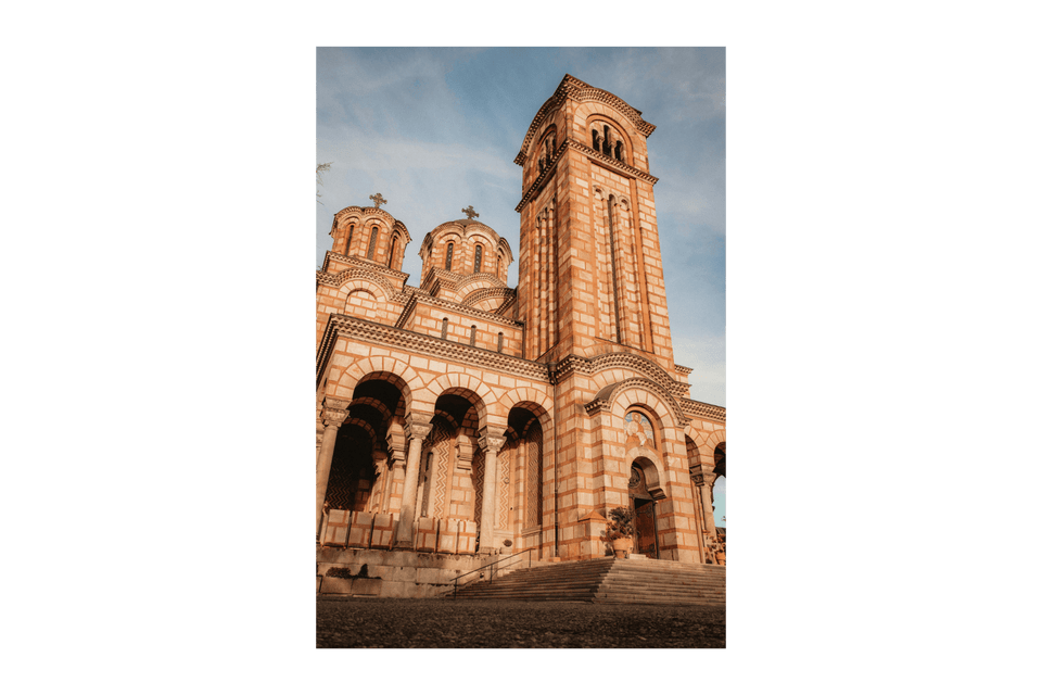 Una vista dal basso di una chiesa in pietra a strisce, ornata, con più cupole e un alto campanile sotto un cielo parzialmente nuvoloso.