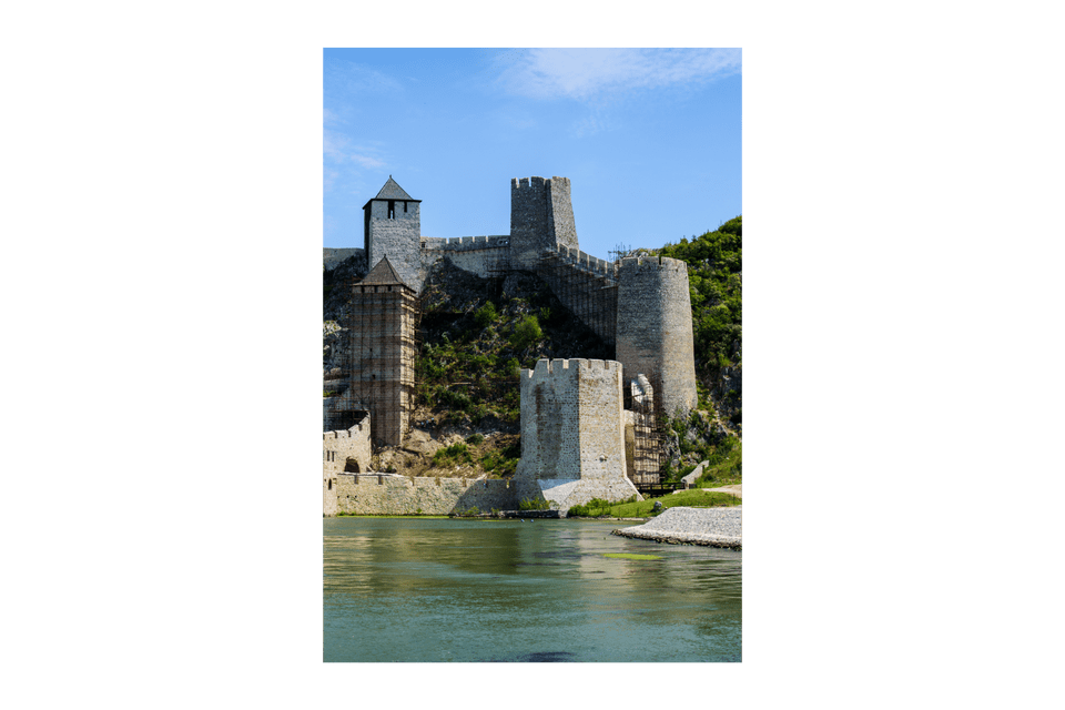 Una fortezza medievale in pietra con torri in restauro su una verde collina lungo un ampio fiume.