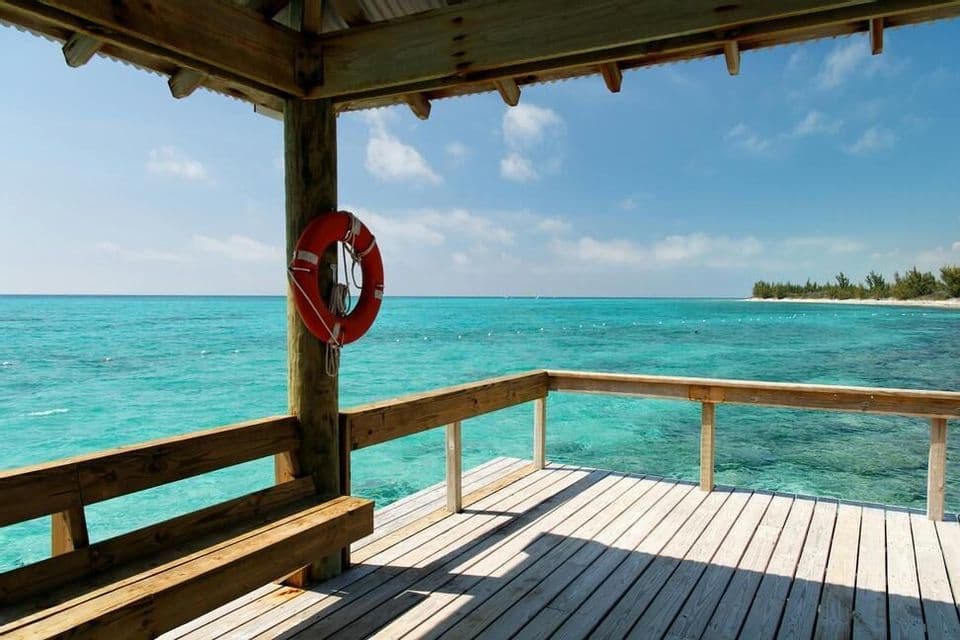 A view from a covered wooden pier with a lifebuoy, looking out over a calm turquoise sea under a blue sky.