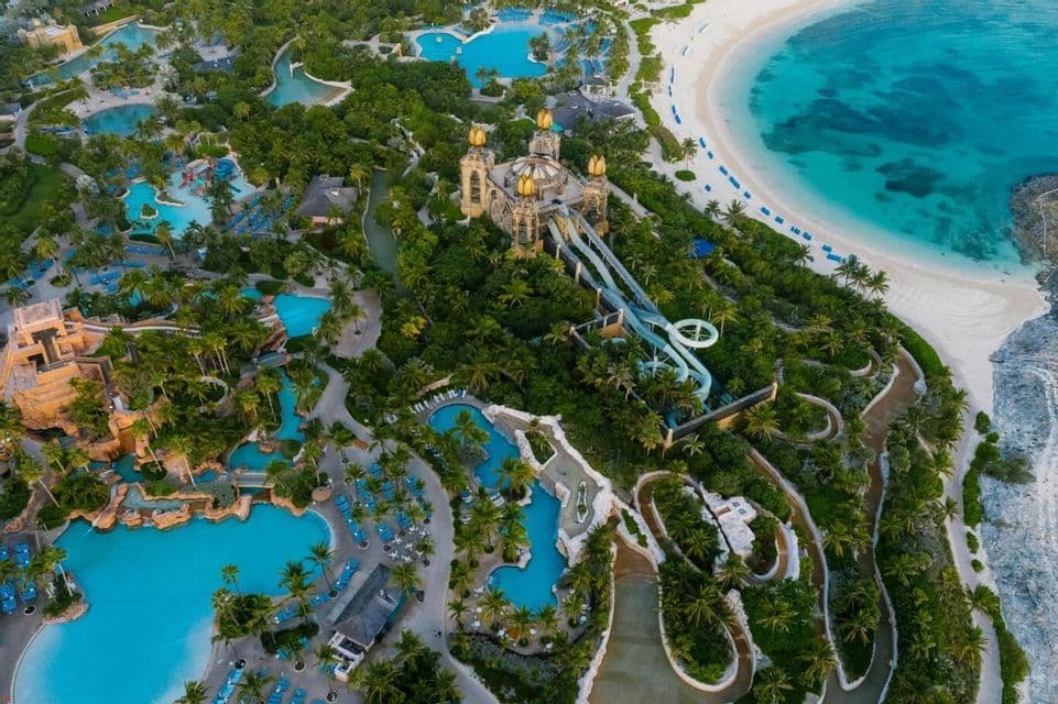 An aerial view of a large water park resort with pools, slides, and a central golden-domed building next to a beach.