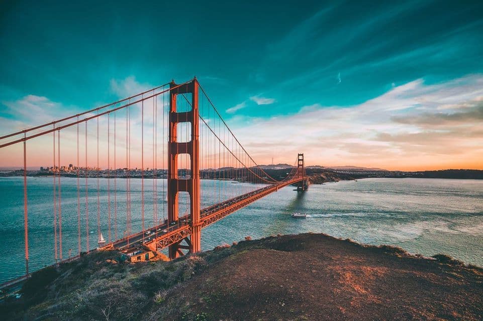 Il Golden Gate Bridge visto da una collina al tramonto, con lo skyline della città visibile in lontananza sull'acqua.