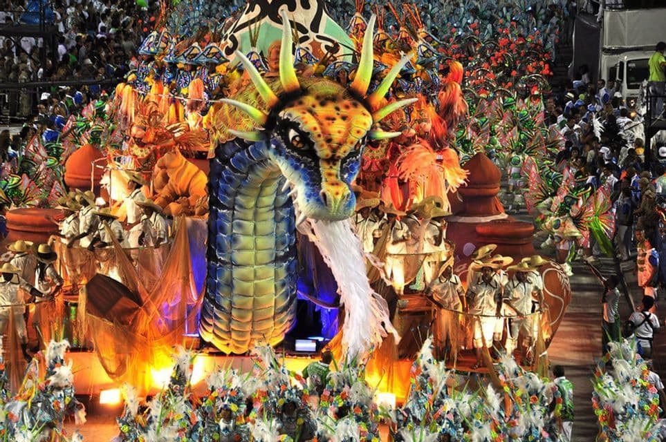 Ein großer, farbenprächtiger Drachenwagen bewegt sich während eines Karnevals durch eine Parade, umgeben von Darstellern in lebhaften Kostümen.