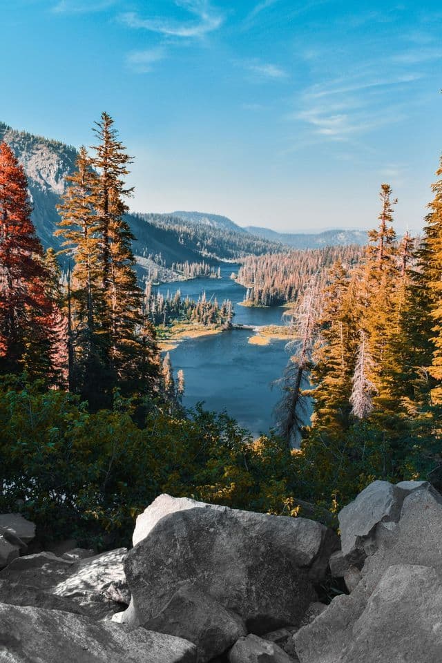 A view from a rocky outcrop over a series of blue lakes in a valley surrounded by mountains and pine trees with autumn colors.